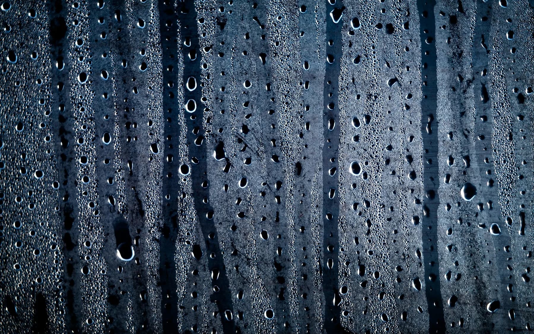 Rain and moisture droplets streaking down a dark glass surface