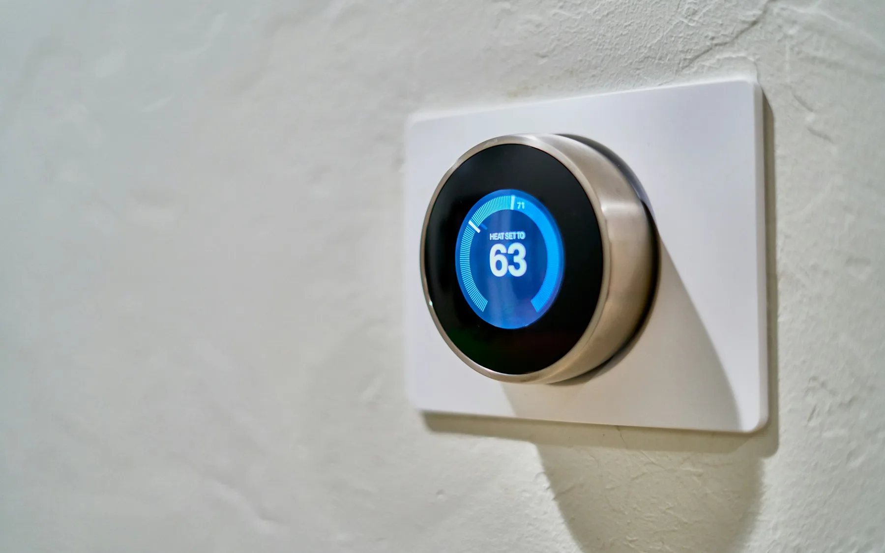 Wall-mounted smart thermostat displaying an indoor temperature of 63 degrees