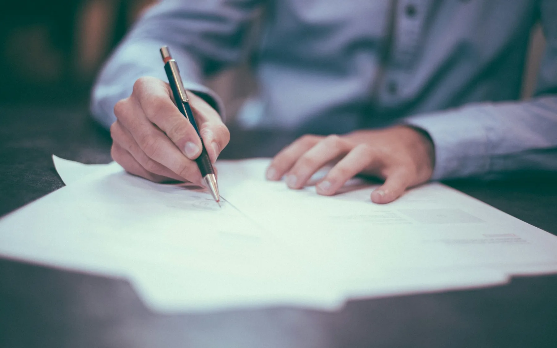 Person writing and reviewing terms on printed paperwork at a desk